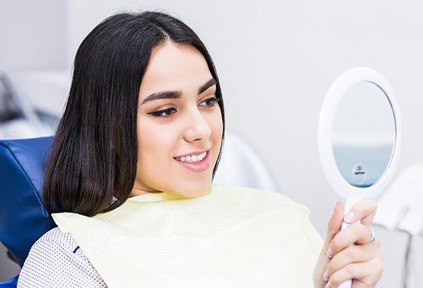 Woman looking at smile in mirror after metal free dental restoration