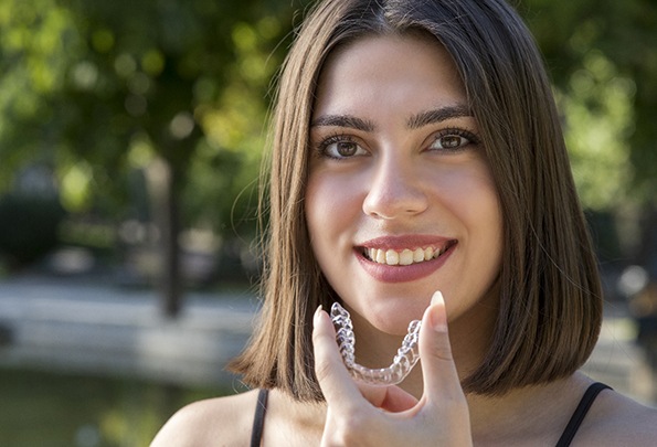 A young woman with dark hair holding an Invislaing clear aligner