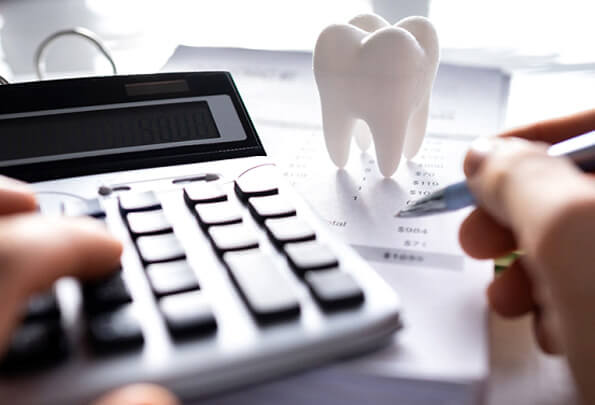 model of tooth on an invoice next to a person calculating cost at a work desk